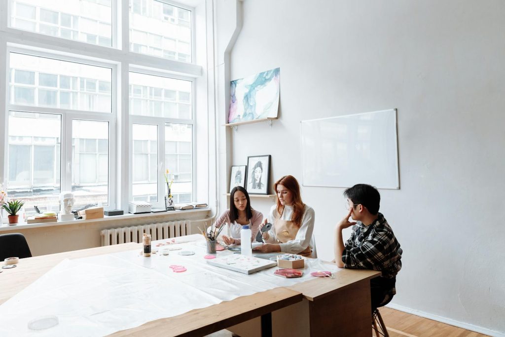Three individuals engage in a creative art session in a modern studio with natural light.